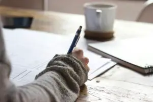 Why I’m taking the Data+ Certification Exam hand holding a pen writing on papers on a desk. Coffee cup sitting on desk in the background.