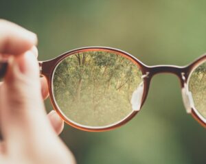 Projects Hand holding red glasses. Image in the lens is clear, image outside the lens is blurry.