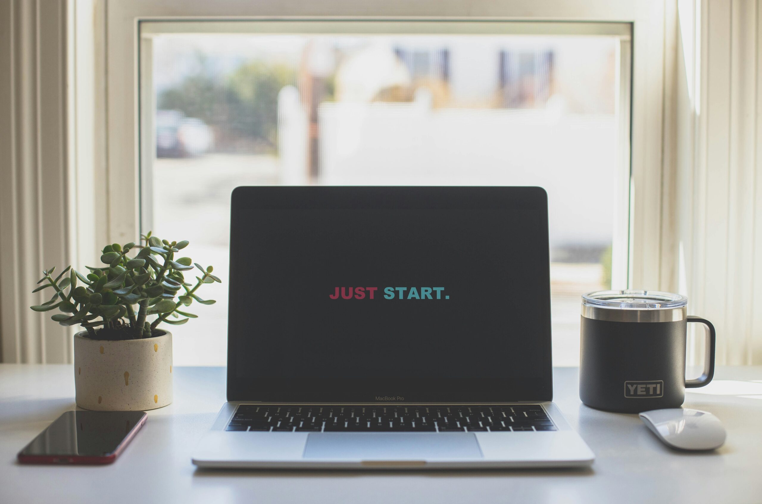 Home Silver laptop sitting on a desk with a black screen with "Just Start" on the screen.