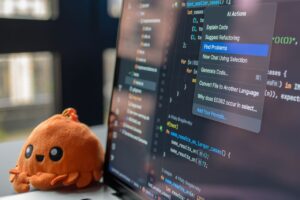 pexels photo 34804015 34804015 A laptop screen showing a code editor with a cute orange crab plush toy beside it.