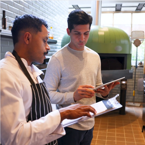 a chef stands next to a business owner looking at a clipboard.webp
